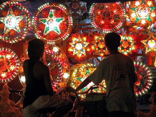 Two people looking at vibrant illuminated Filipino star parols displayed at night