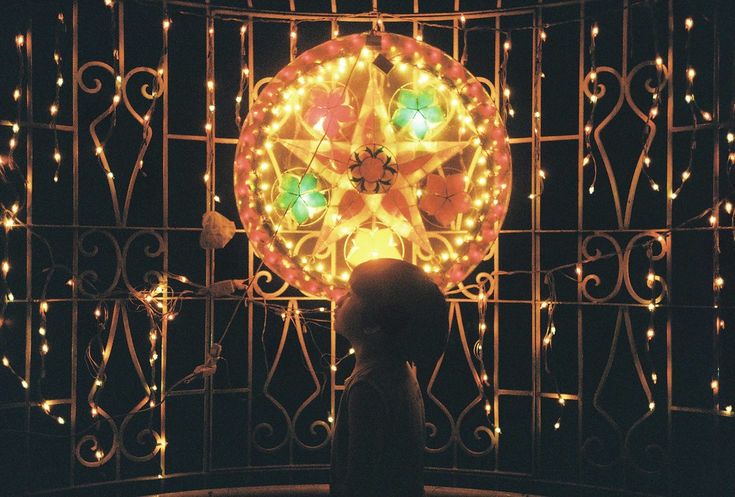 Silhouette of a young child looking up in wonder at a bright glowing Filipino parol lantern