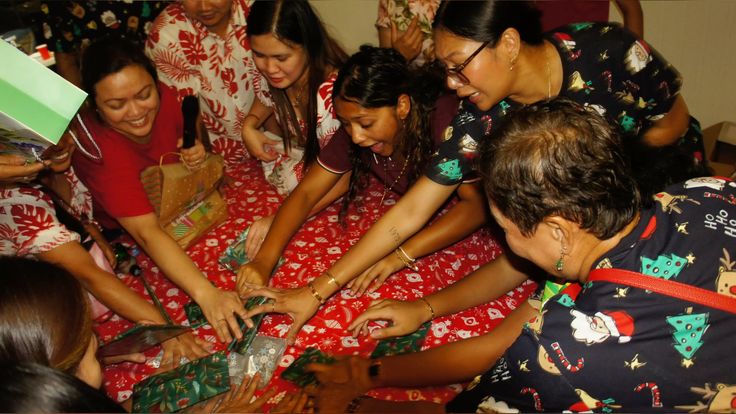 Filipino family laughing and reaching for gifts on a bed during a holiday reunion
